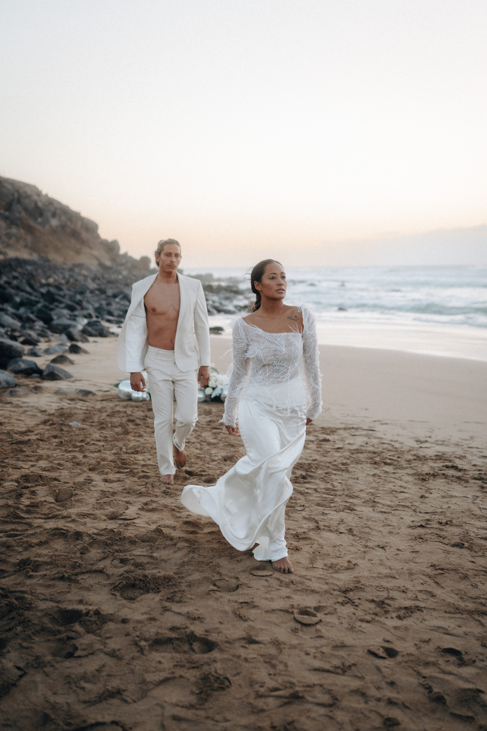 Ein Hochzeitspaar läuft nach Sonnenuntergang am Strand entlang.