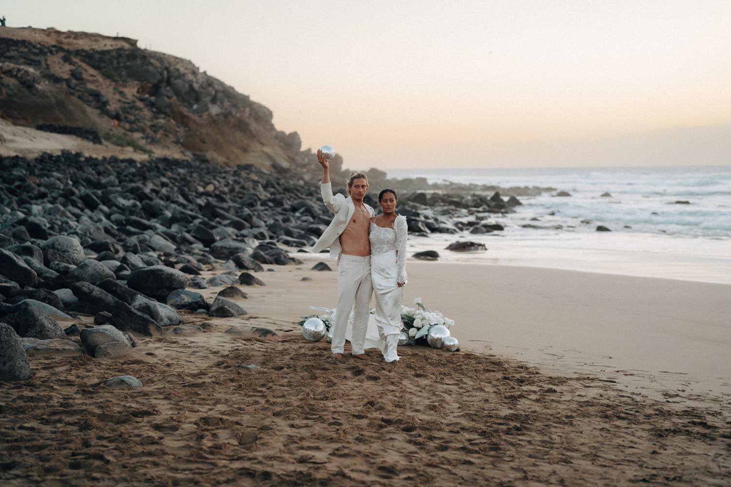 Ein Brautpaar im Disko-Hochzeitsstil steht kurz nach Sonnenuntergang am Strand von Fuerteventura.