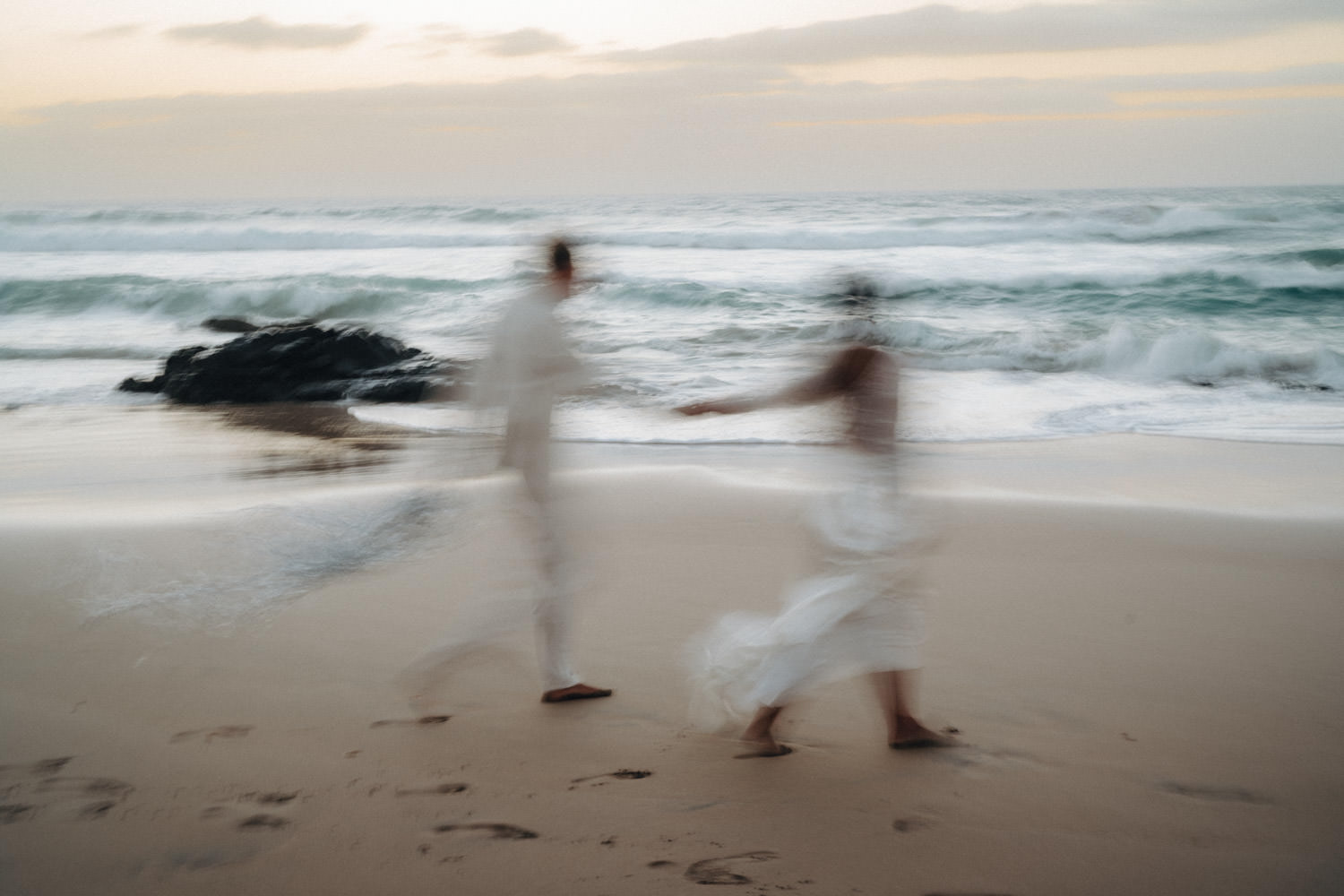 Ein Brautpaar rennt am Strand von Fuerteventura im Sonnenuntergang entlang und ist verschwommen fotografiert.