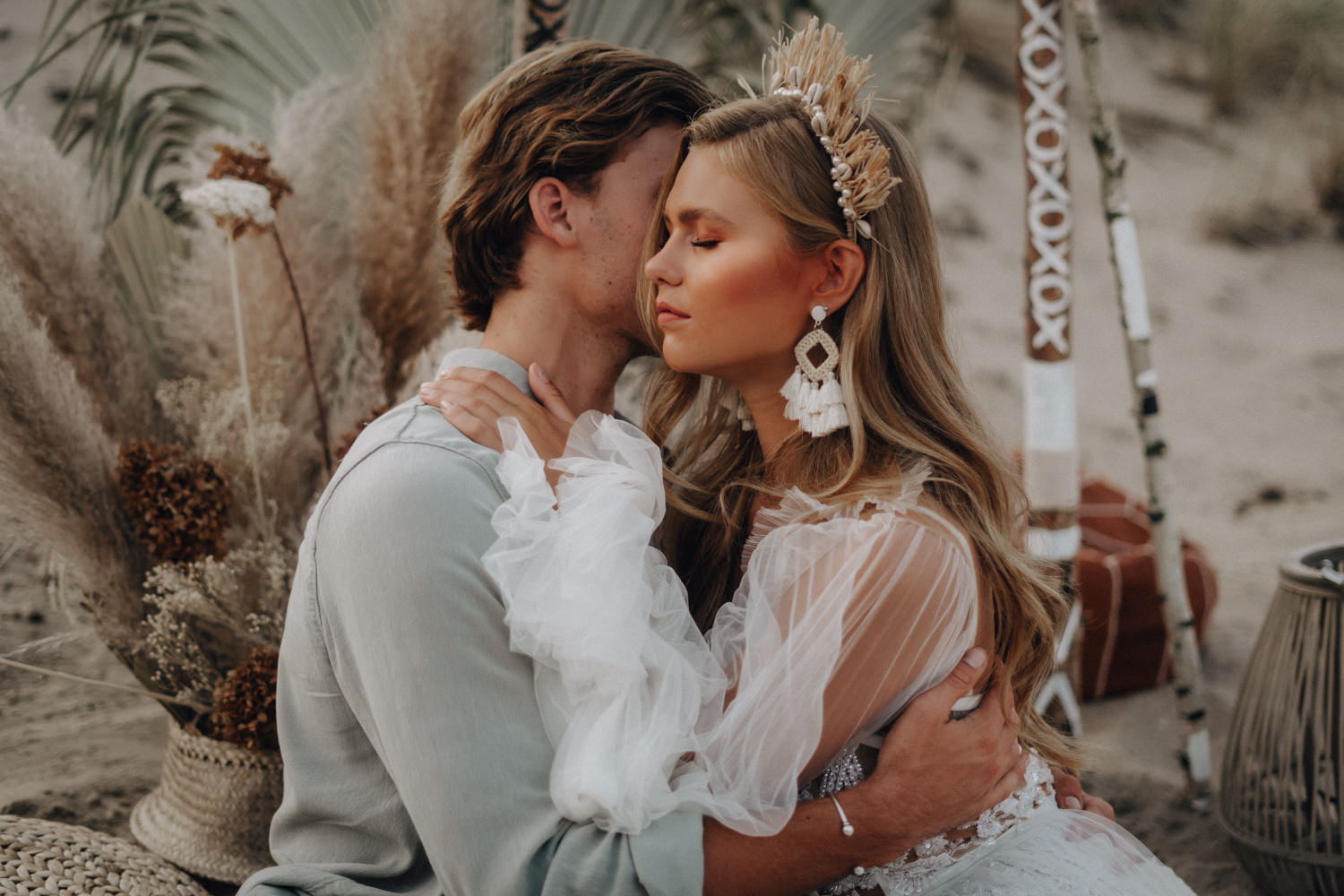 Ein Paar im Boho Style sitzt im Sand und kuschelt