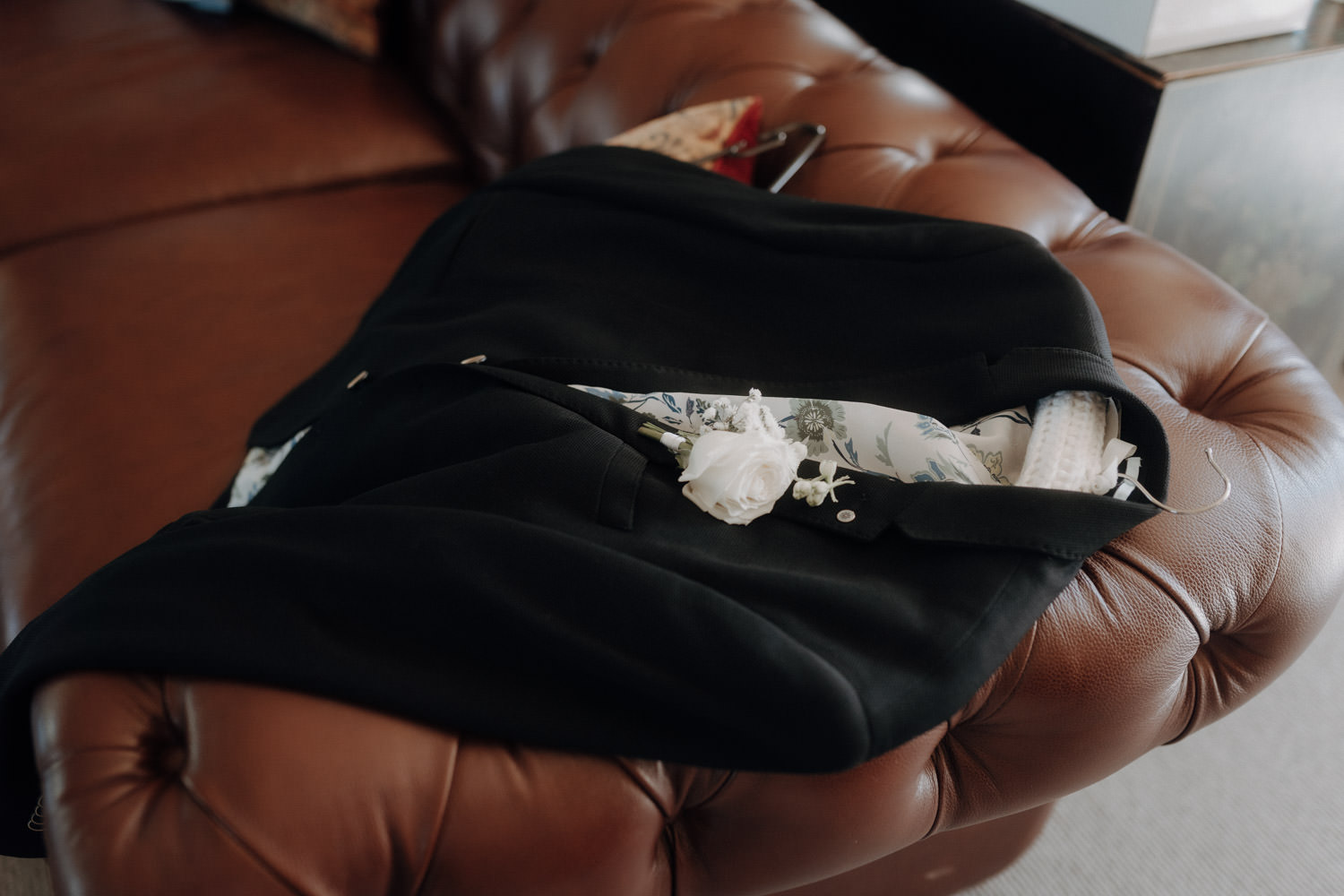 Das Jacket des Bräutigams liegt beim Getting Ready auf einer Ledercouch.