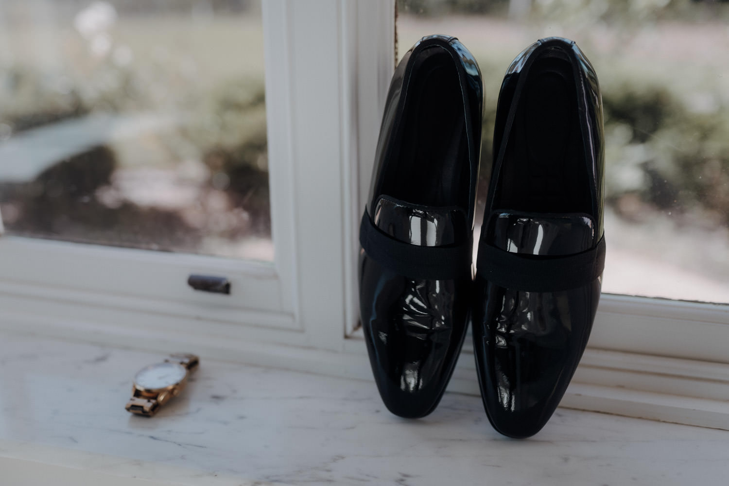 Bräutigam-Schuhe und eine Uhr sind beim Getting Ready für Detailsfotos am Fenster drapiert.